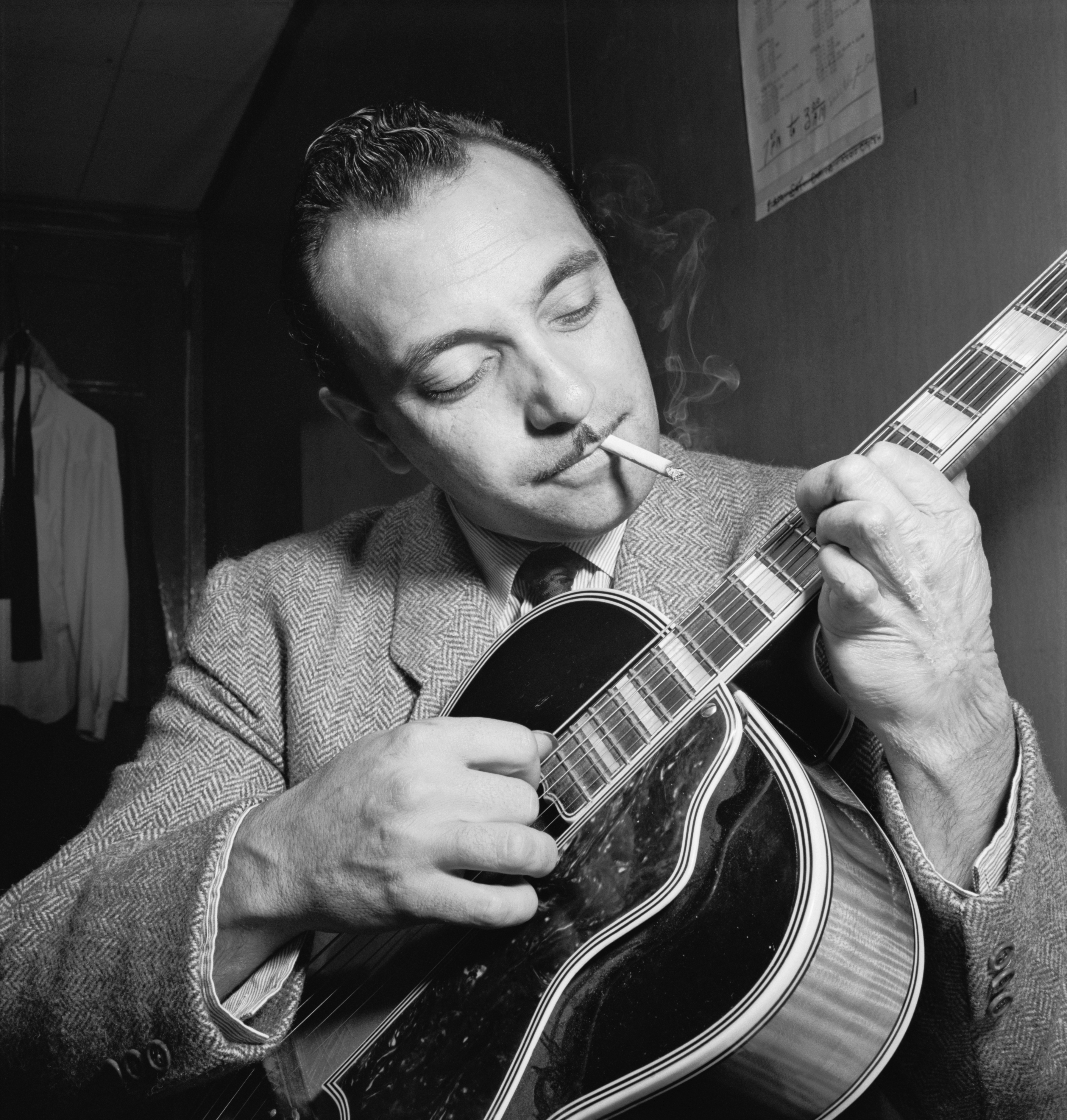 Django Reinhardt playing an archtop guitar with a cigarette between his lips at the Aquarium, New York, circa November 1946.