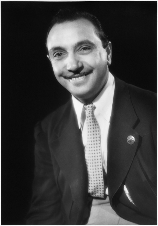 Django Reinhardt smiling in a seated Studio Harcourt portrait.